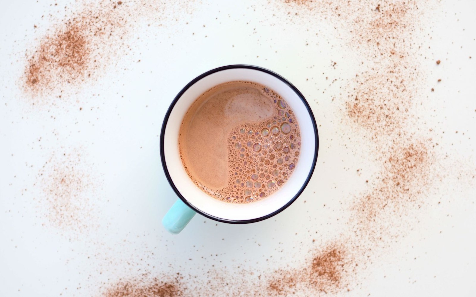 Overhead view of a foamy hot chocolate in an enamel mug with cocoa powder scattered around