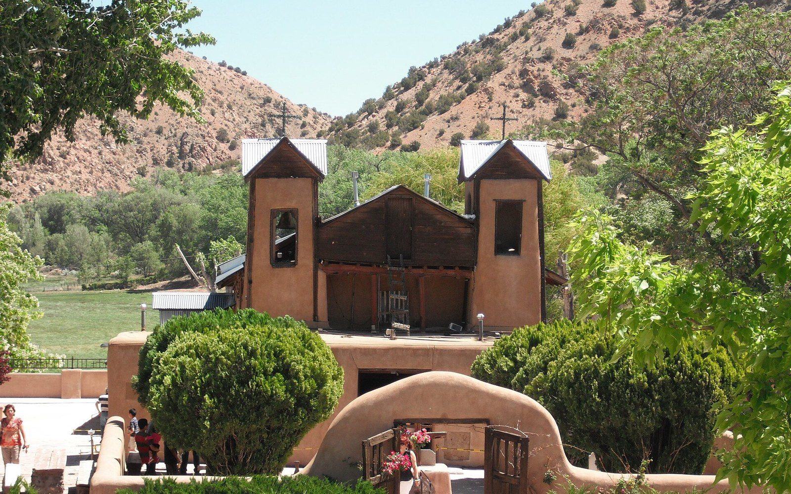 Adobe church with twin bell towers nestled between desert hills and greenery